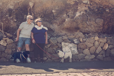 Full length of mature couple standing with dogs against wall