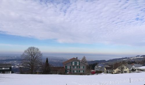 Snow covered houses by buildings against sky