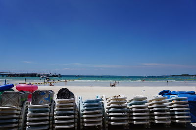 Stack of deck chairs on beach against clear blue sky