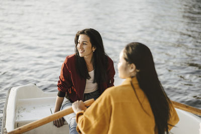 Smiling woman sitting with female friend rowing boat on lake