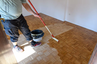 Side view of man using roller to apply lacquer clear coat to hsrdwood floor