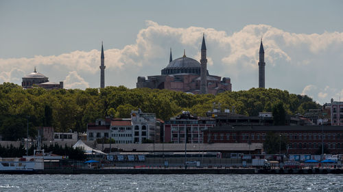 Buildings at waterfront against cloudy sky