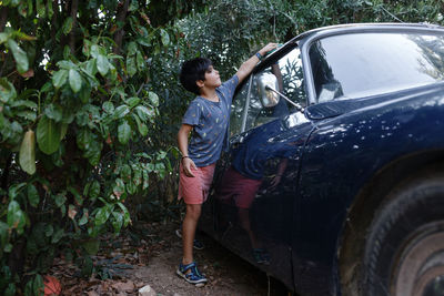 Girl with short black haircut washing blue car in the garden