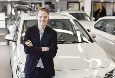 Portrait of happy male customer leaning on car at showroom