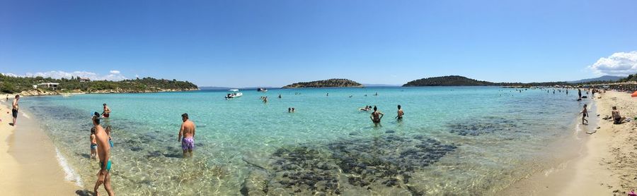 Panoramic view of people on beach against clear blue sky