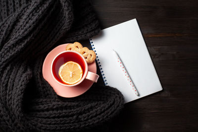 Clear copybook, cup of pomegranate tea, pen and knitted scarf on black wooden background