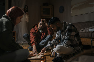 Friends touching ouija board while ghost in background at cabin