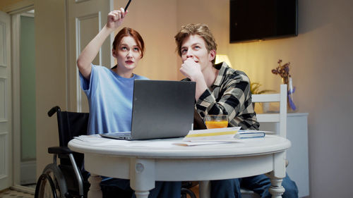 Young couple looking away siting next to laptop
