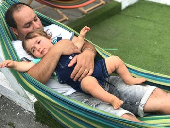 High angle view of father embracing baby boy while lying in hammock