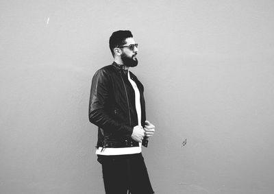 Young man looking away while standing against wall