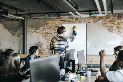 Businessman sticking adhesive notes and conducting business meeting with computer programmers in office