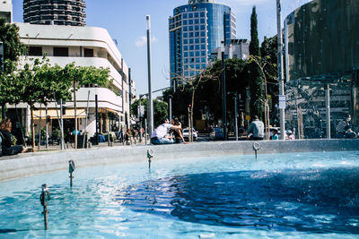 People swimming in pool against buildings in city