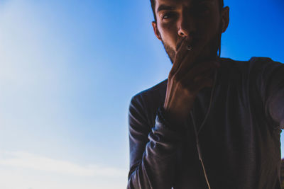 Portrait of man smoking cigarette against blue sky