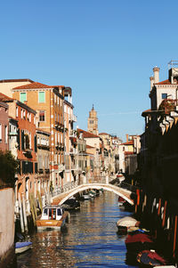 Bridge over canal amidst buildings in city against clear sky