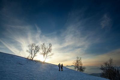 Hikers walking on snow covered hill against sky during sunset