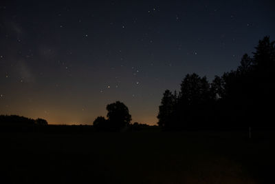 Silhouette trees on field against sky at night