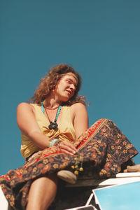 Low angle view of young woman sitting against blue sky