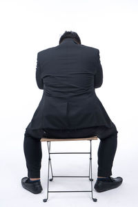 Rear view of man sitting on chair against white background