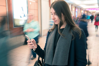 Young woman using mobile phone while standing on laptop