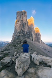 Rear view of man sitting on rock against sky