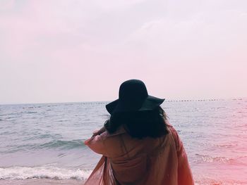 Rear view of woman standing on beach against sky during sunset