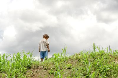 Rear view of boy standing on field against sky