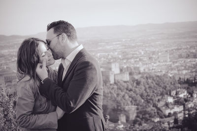 Man kissing woman while standing against cityscape