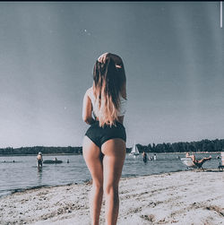 Rear view of woman standing on beach against sky