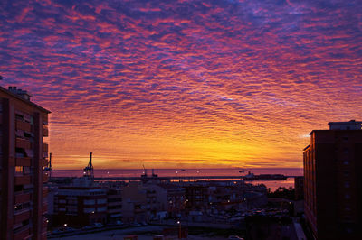 Buildings in city against dramatic sky during sunset