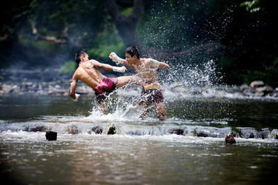 Full length of shirtless warriors fighting in river at forest