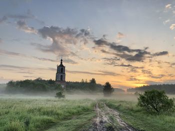 Lighthouse on field against sky during sunrise 