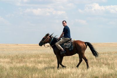 Portrait of man riding horse on field against cloudy sky