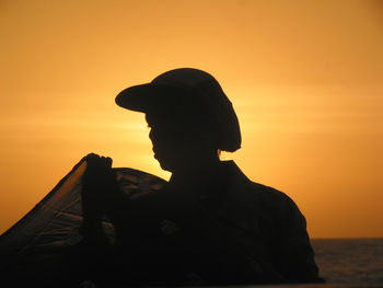 Silhouette man sitting on sea against orange sky