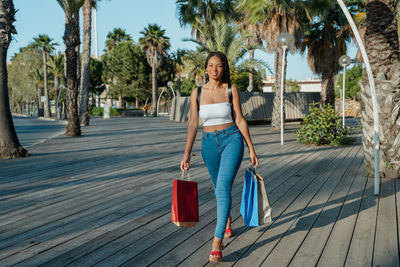 Cheerful young african american female buyer with shopping bags looking away while walking on street