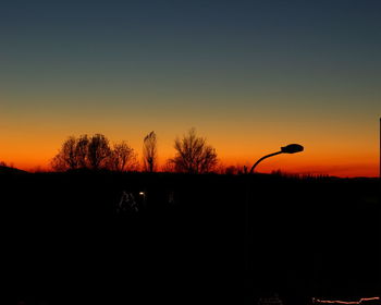 Silhouette trees on field against orange sky