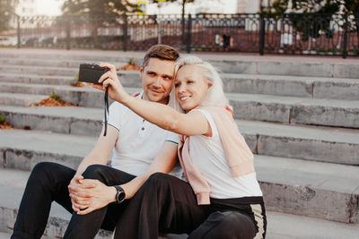 Smiling couple taking selfie while sitting on staircase