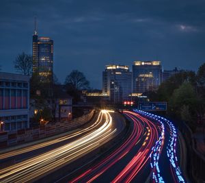 Light trails on road amidst buildings against sky at night