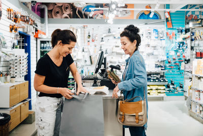 Female cashier talking assisting customer at checkout counter in store