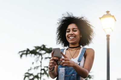 Smiling young woman using mobile phone against sky