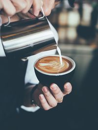 Cropped hand of woman pouring milk in cappuccino