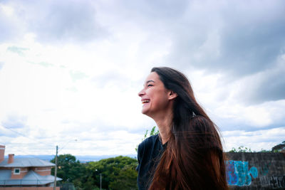Low angle view of happy beautiful woman against cloudy sky