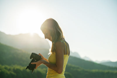 Side view of woman photographing on mountain against sky