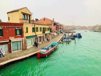 Boats moored in canal by buildings in city against sky