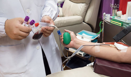 Doctor collecting samples while man donating blood in hospital