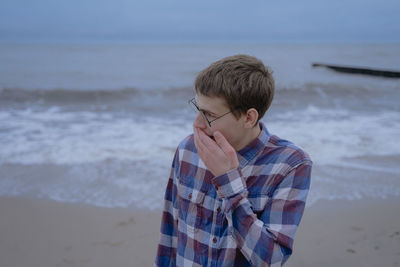 Teenager from surprise covered his mouth with his hand, stands on the seashore in a shirt and 