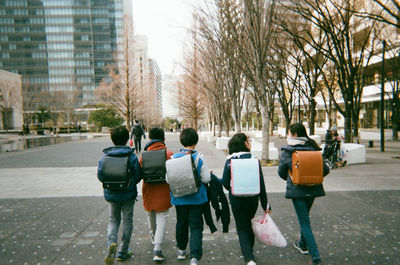 Rear view of backpack people walking on street in city