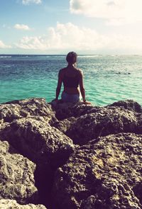 Young woman standing on rock at sea shore against sky