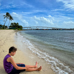 Rear view of woman standing at beach against sky