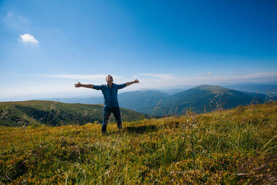 Man with arms outstretched on field against sky