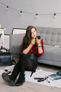 Young caucasian woman in a red plaid shirt and skirt does her makeup, paints her lips with glitter